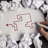 Graph paper with red, maze like line drawn along it and crumpled up papers around it.