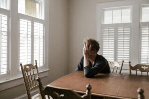 A man sits alone at a table in a bright room, displaying deep emotion