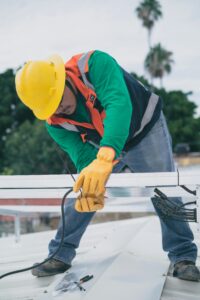 A construction worker installs electrical equipment on a roof.