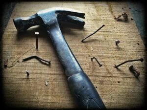 A weathered hammer surrounded by bent nails on a wooden plank