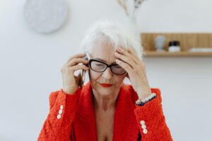 Senior woman in red blazer stressed while talking on the phone indoors.