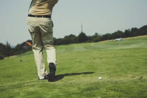 Golfer taking a swing on a sunny day, showcasing leisure and sport on a lush golf course.